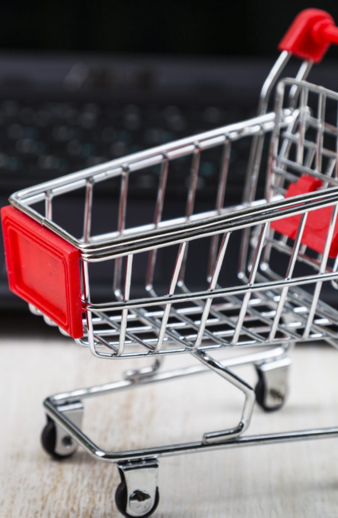 An empty miniature shopping cart in front of a black computer keyboard.