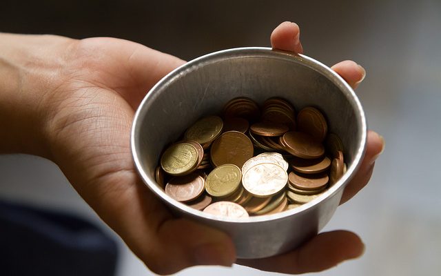 A hand holding a tin filled with change.