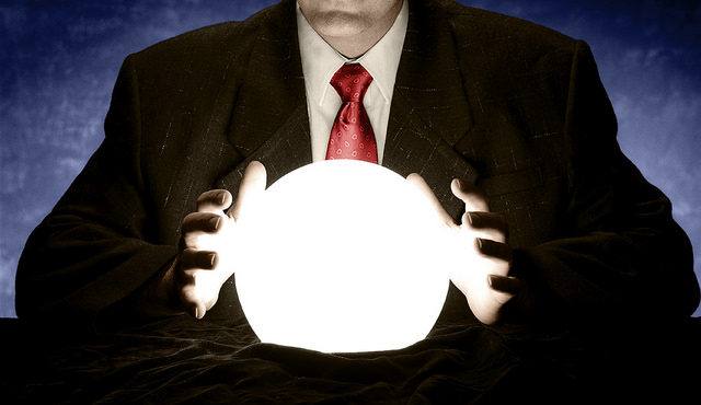 A man in a business suit holds his hands near a crystal ball.