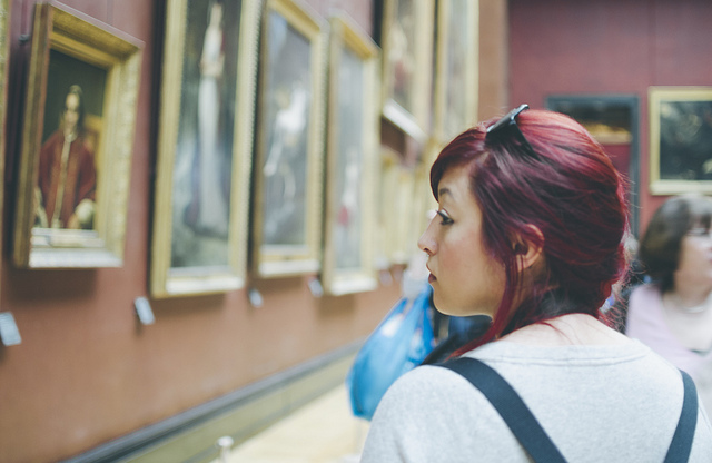 A young woman browses paintings at an art museum.
