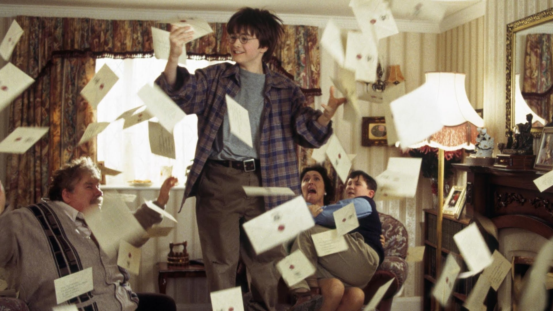 Young Harry Potter jumps to catch one of many letters floating in the air around his living room as his Muggle family looks on in horror.