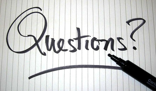 A black marker has written “Questions?” across a piece of notebook paper.