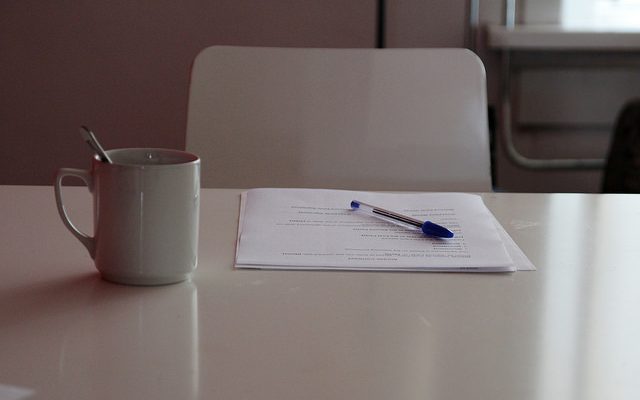 A pen sits on top of a printed out grant next to a cup of coffee.